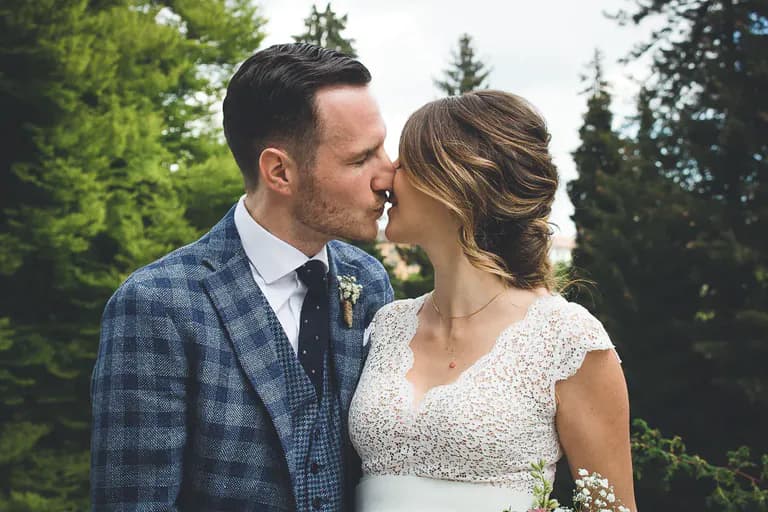 Hochzeitspaar küsst sich in der Natur mit einem Wald im Hintergrund